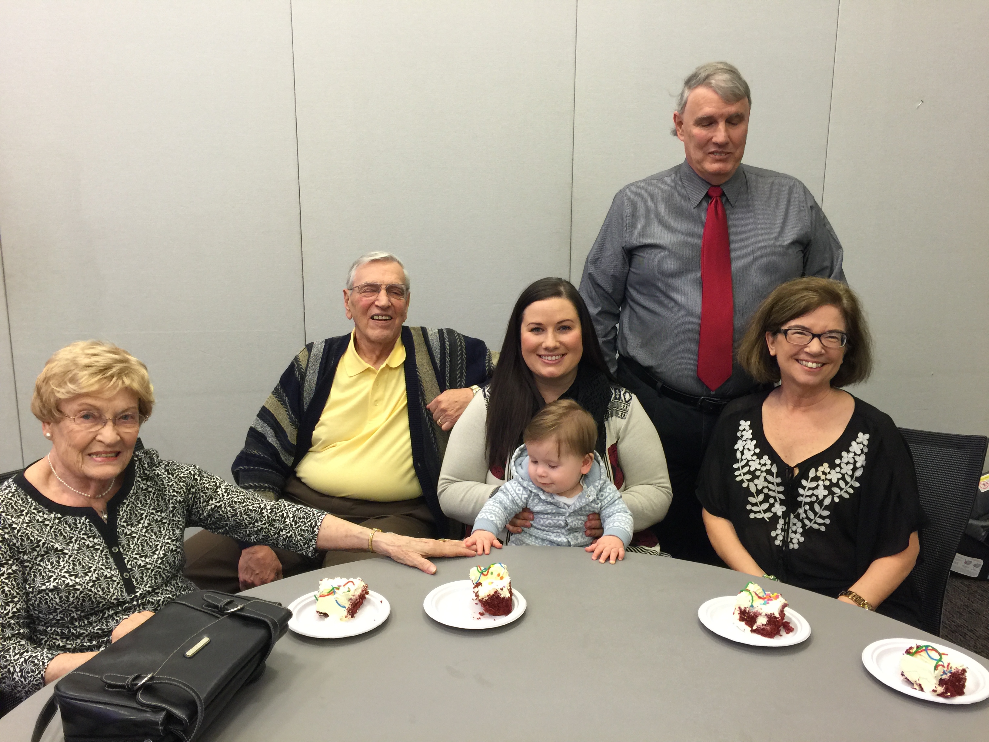 Bill Pasco and his family sitting at a table.  His wife, parents, and daughter with baby on her lap.