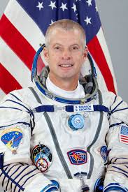 Photo of Steve Swanson in his astronaut uniform in front of a draped American flag