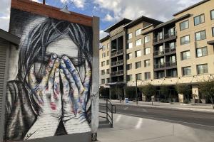 A mural of a woman holding her face in her hands in front of a new apartment complex