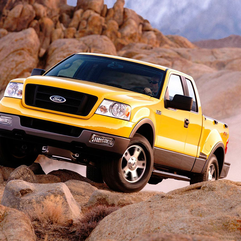 A yellow Ford F150 truck drives over boulders in the wilderness