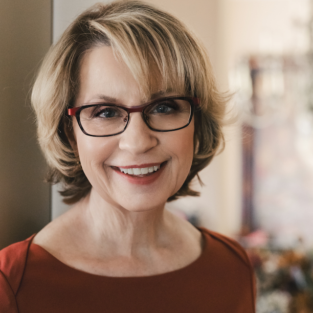 woman with short blond hair, dark rimmed glasses wearing a red sweater